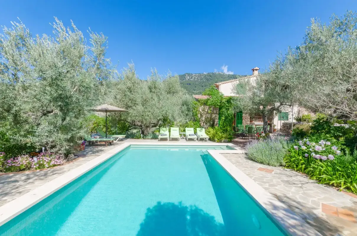 An outdoor swimming pool is bordered by stone paving, greenery, and lounge seating.