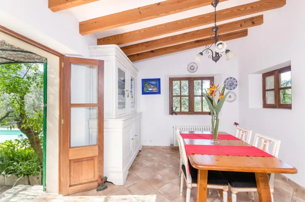 A dining room with a long table and exposed wooden ceiling beams.