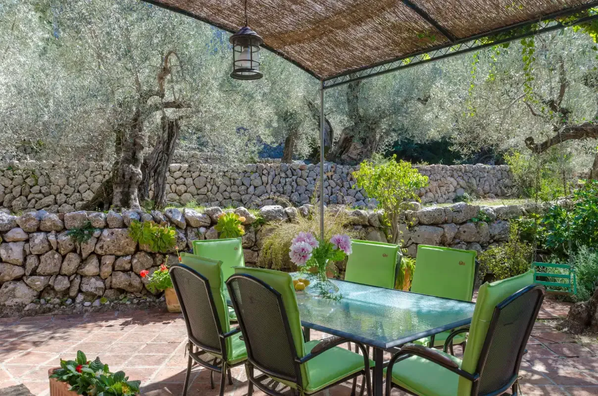 A shaded outdoor dining area has a glass table surrounded by green seating.