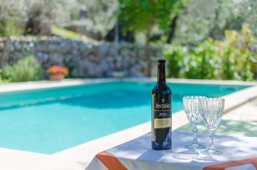 A swimming pool beside a table set with a wine bottle and glasses.
