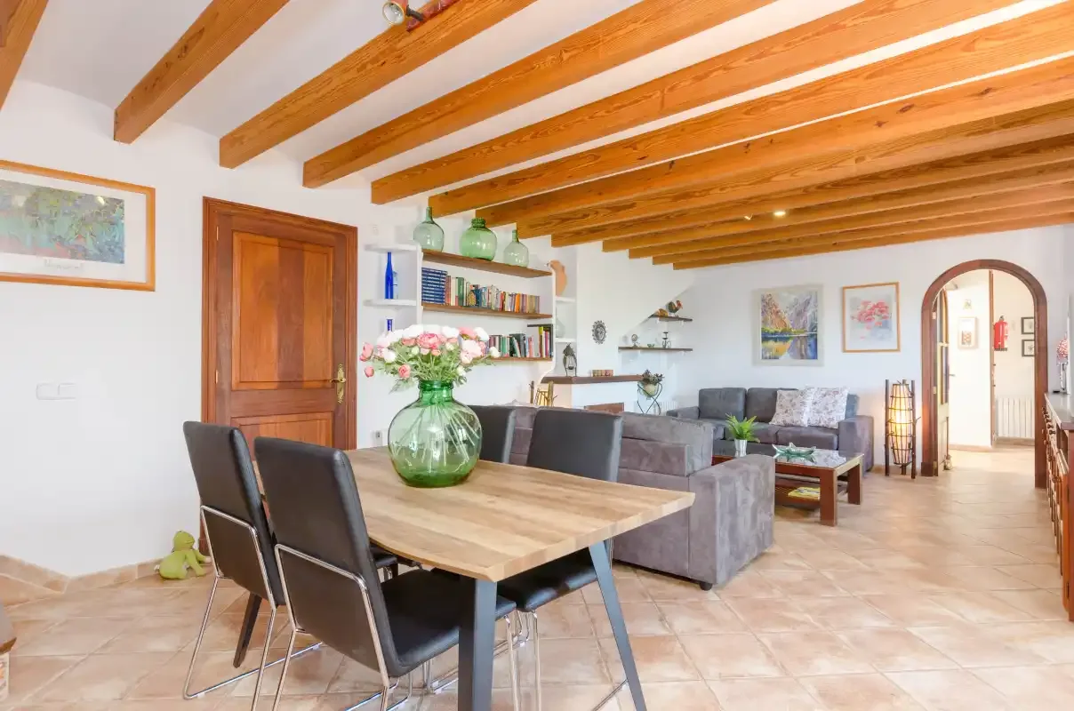 A dining and living area with a wooden table, seating, and exposed ceiling beams.