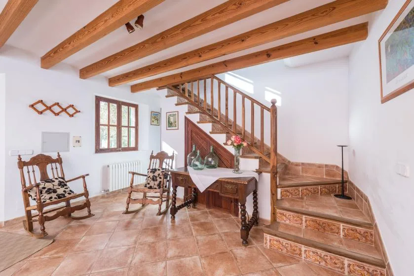 A rustic interior with a wooden staircase, dining table, and exposed ceiling beams.