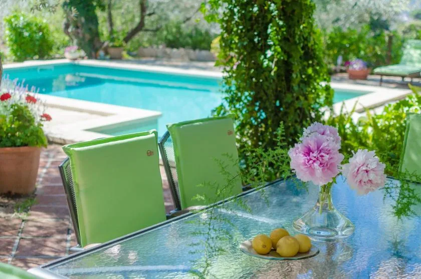 A glass patio table with green seating overlooks a swimming pool.