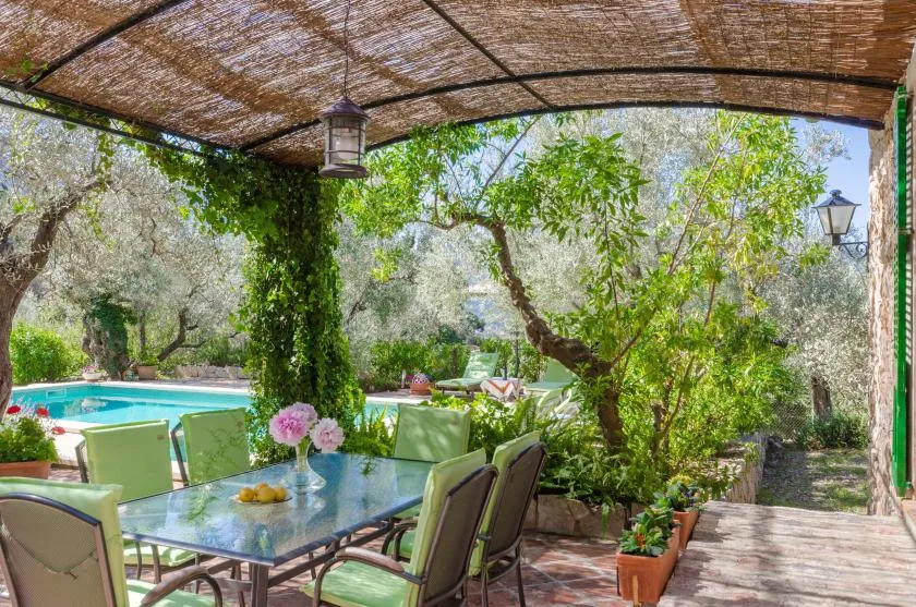A shaded outdoor dining area overlooks a garden and swimming pool.