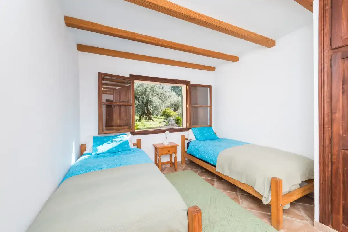 A bedroom with two beds and a window overlooking greenery.