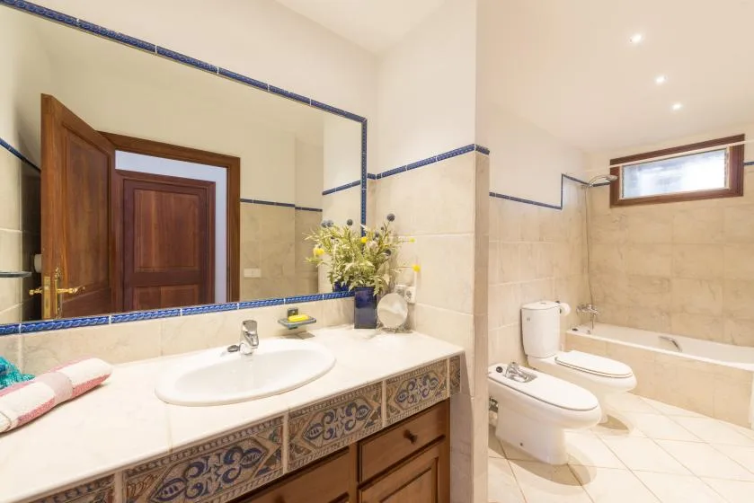 A bright tiled bathroom with a long vanity, mirror, and bathtub.
