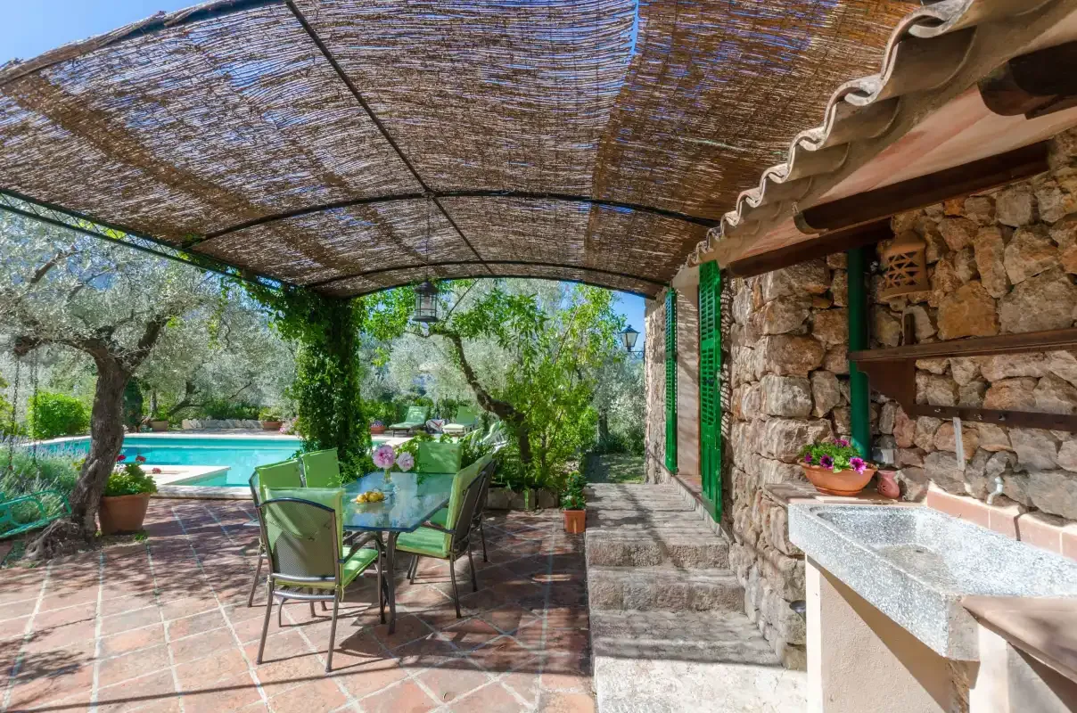 A shaded outdoor dining area opens onto a garden and swimming pool.