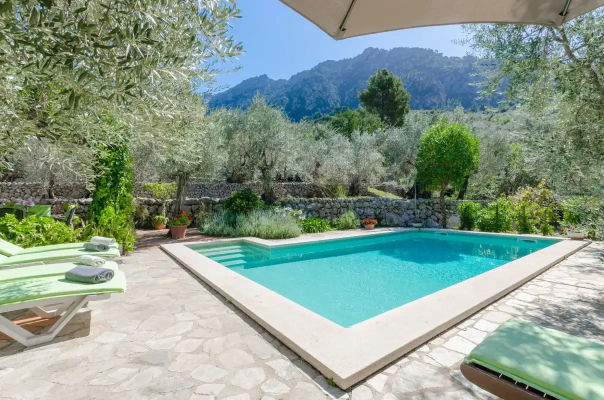 An outdoor swimming pool sits beside a stone patio and garden.