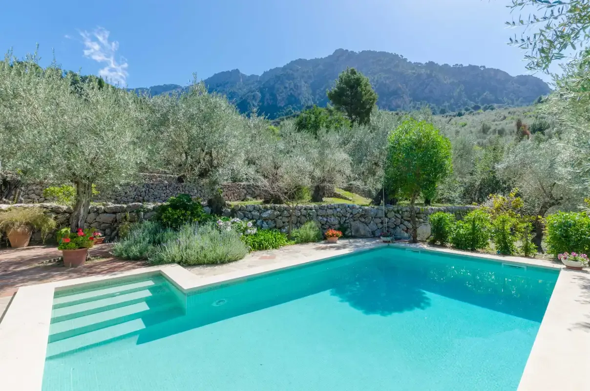 An outdoor swimming pool sits among greenery with mountains in the background.