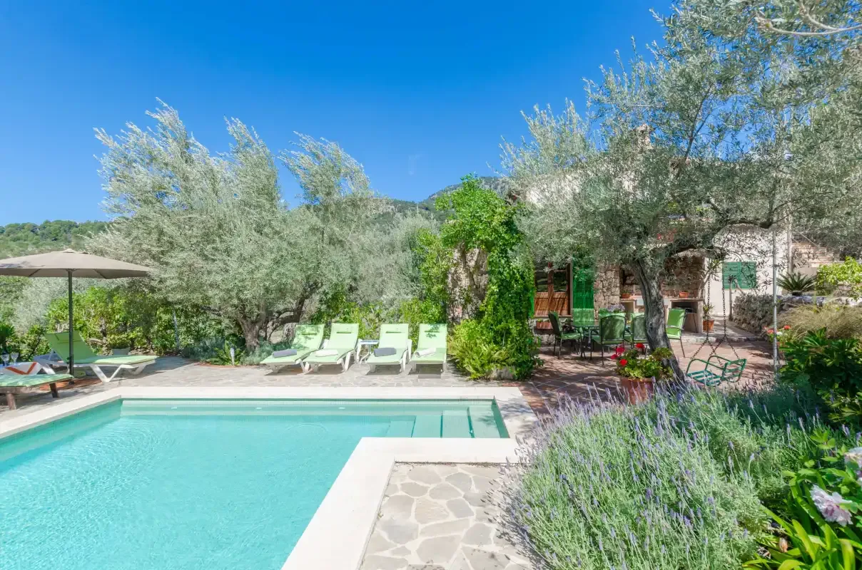 An outdoor swimming pool bordered by lounge chairs, trees, and garden plants.
