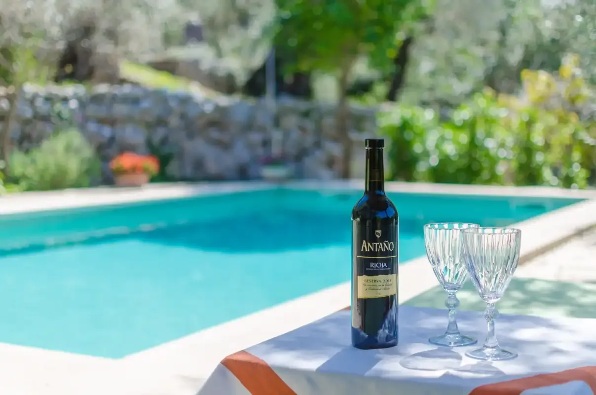 A swimming pool beside a table set with a wine bottle and glasses.