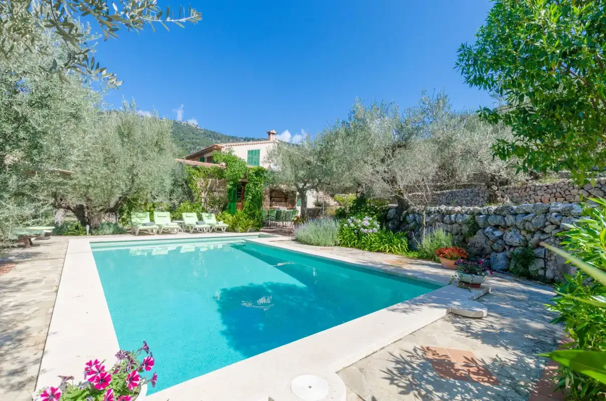 A swimming pool sits beside a stone wall, with trees and seating in the background.