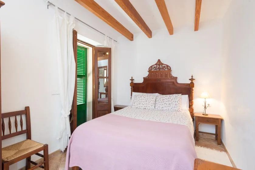 A bedroom with a bed, a wooden headboard, and exposed ceiling beams.