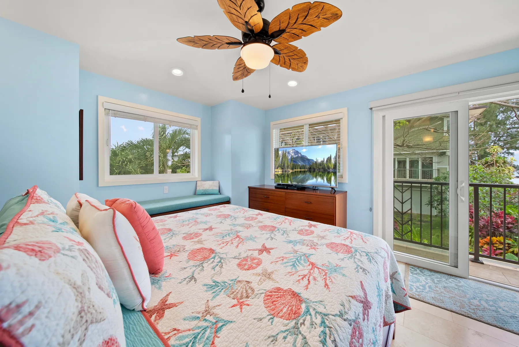 Un dormitorio luminoso con una cama, paredes azules y puertas de cristal hacia un balcón.