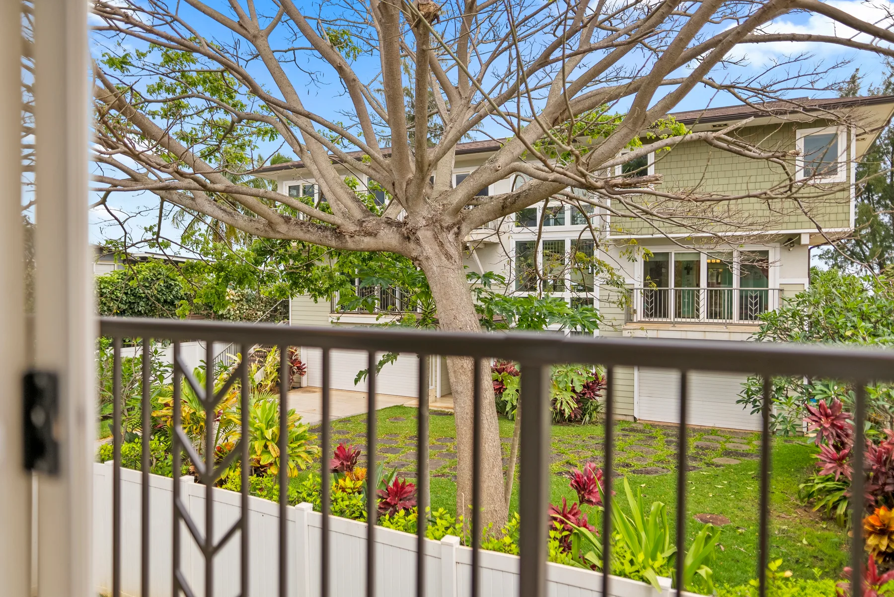 Un jardín frondoso y un árbol grande están frente a un edificio residencial.