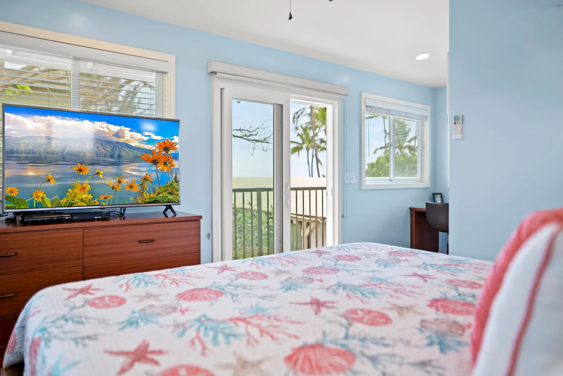 Un dormitorio con una colcha estampada, un televisor y puertas de vidrio hacia un balcón.