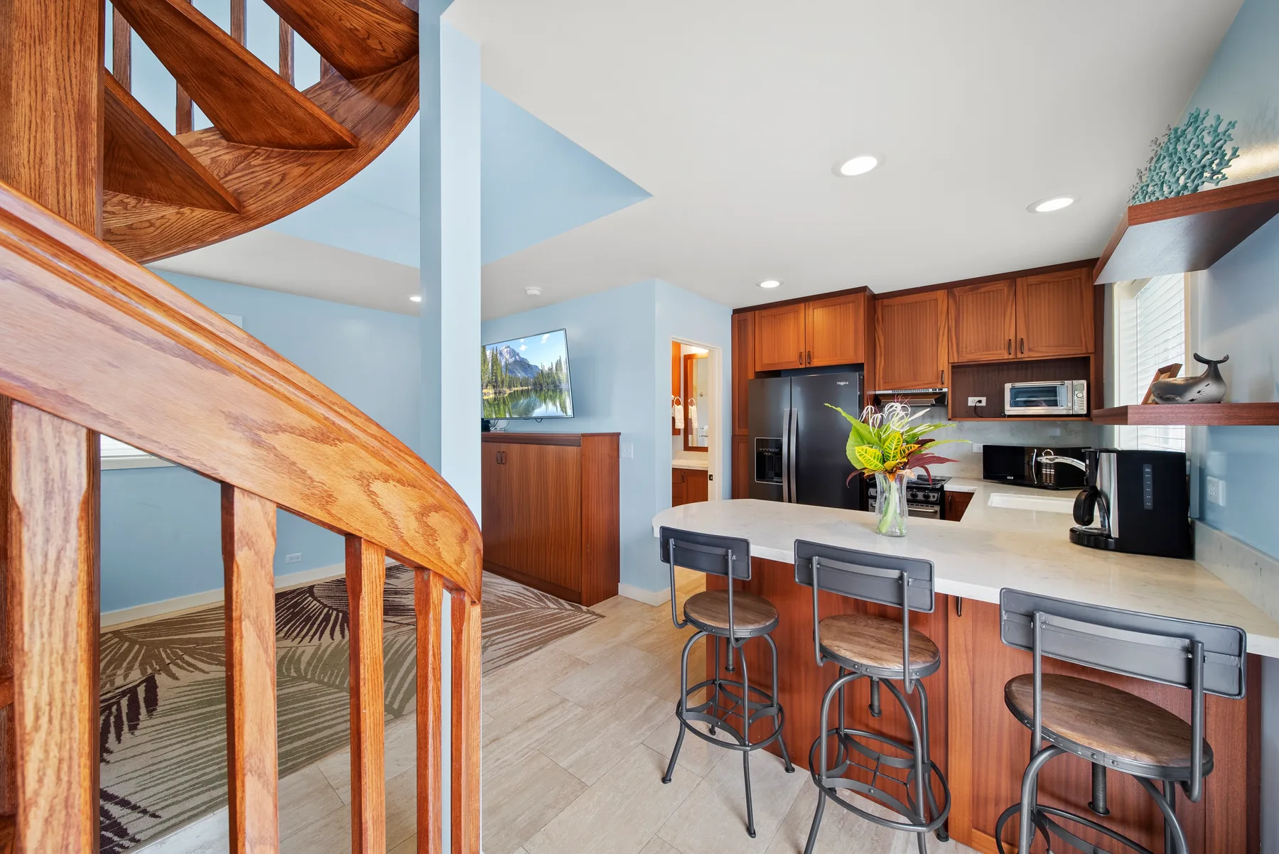 Una cocina con una barra y taburetes está junto a una escalera de madera.