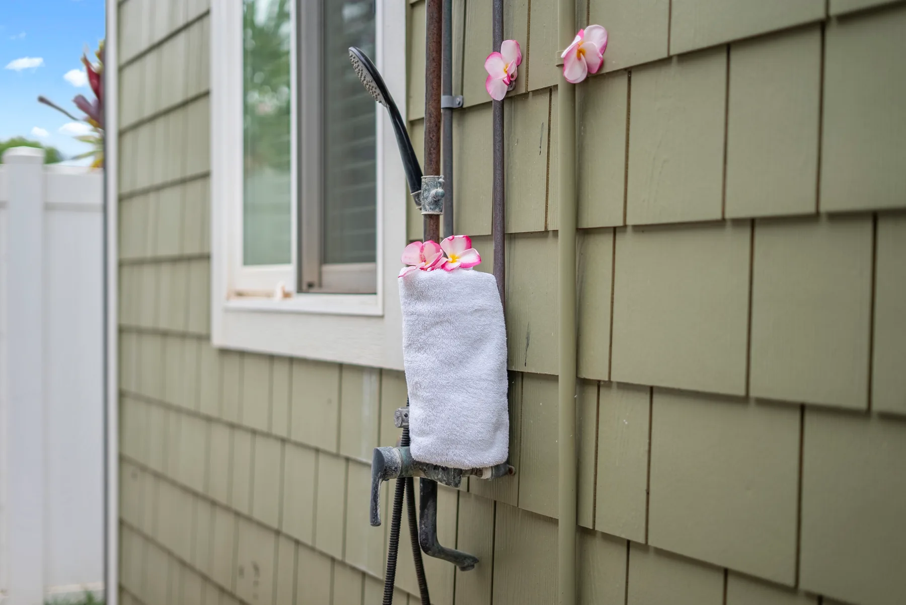 Una toalla cuelga de una ducha exterior junto a una ventana de la casa.