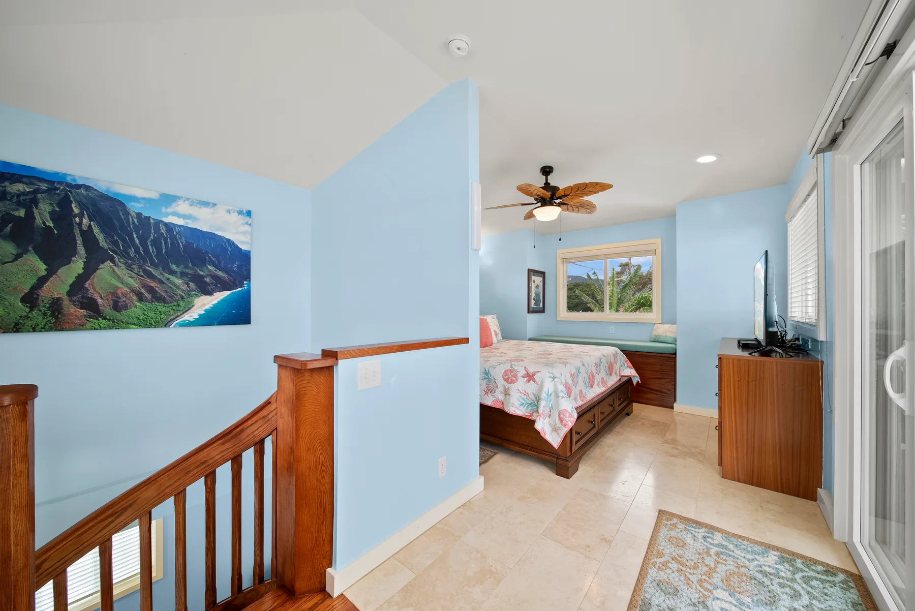 Un dormitorio azul claro con una colcha floral, una ventana y una barandilla de madera.
