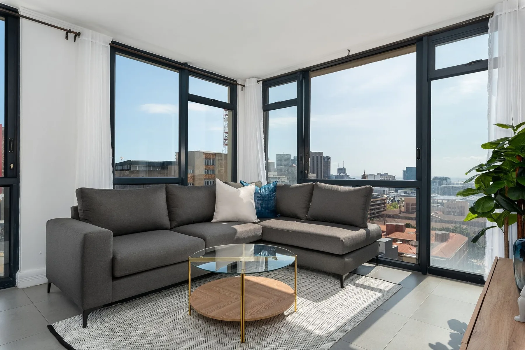 A bright living room has corner windows and a sectional seating area.