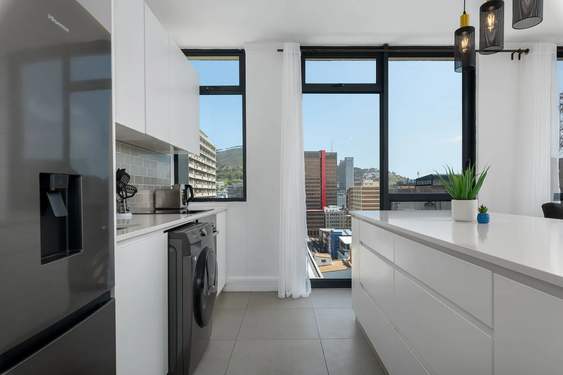 A bright kitchen with white counters and large windows overlooking city buildings.
