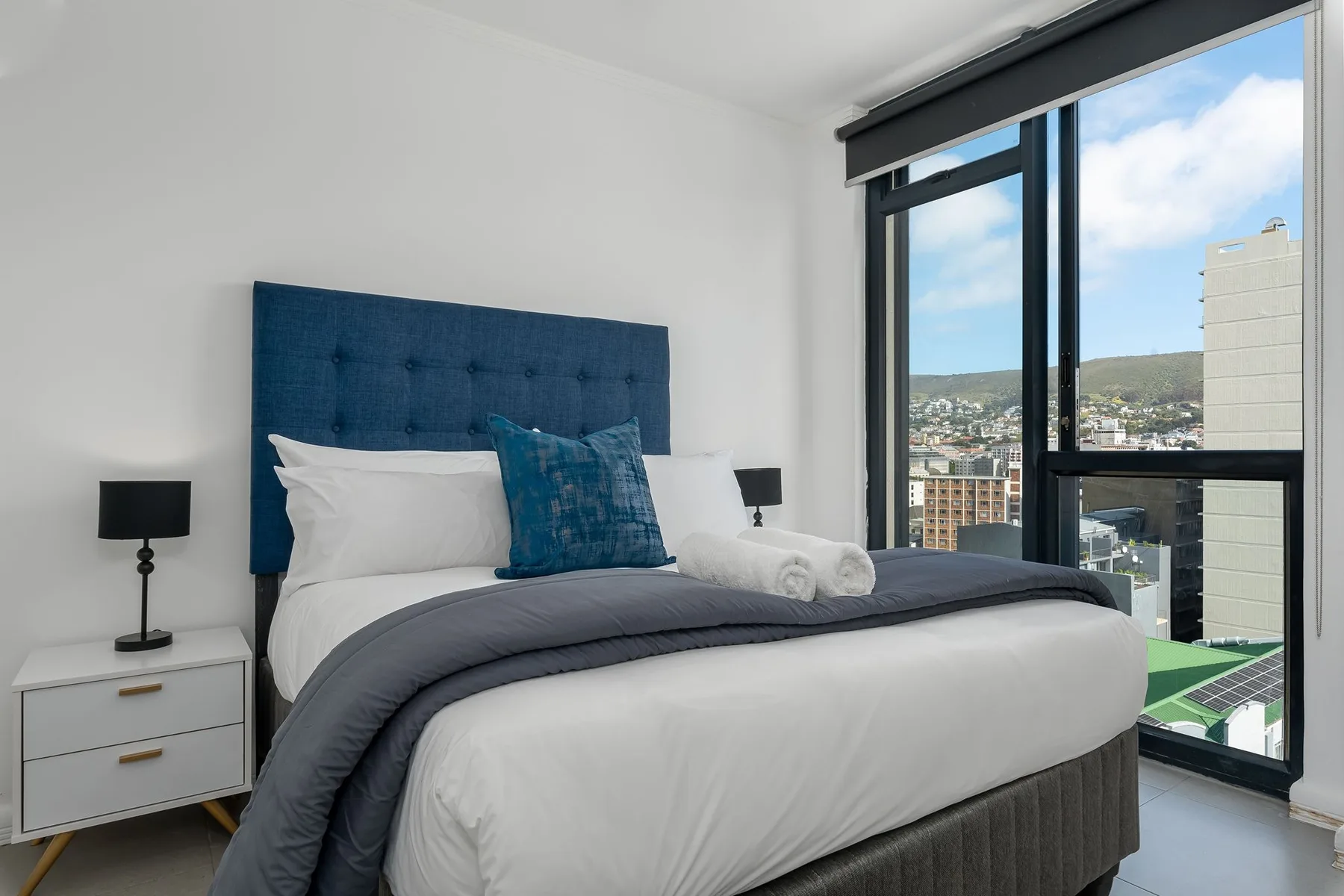 Un dormitorio con una cama bien hecha junto a una ventana grande.