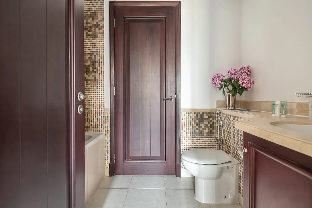 Un baño con azulejos, inodoro, lavabo y puertas de madera oscura.