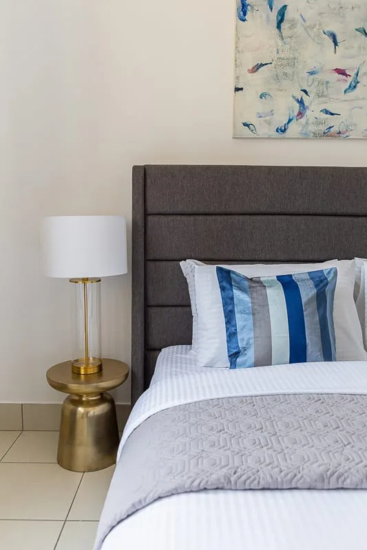 Un dormitorio con una cama bien tendida y una lámpara dorada junto a ella.