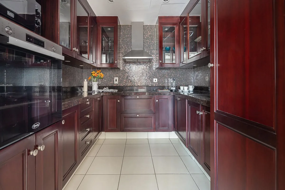Una cocina con gabinetes de madera oscura, salpicadero de azulejos y electrodomésticos empotrados.