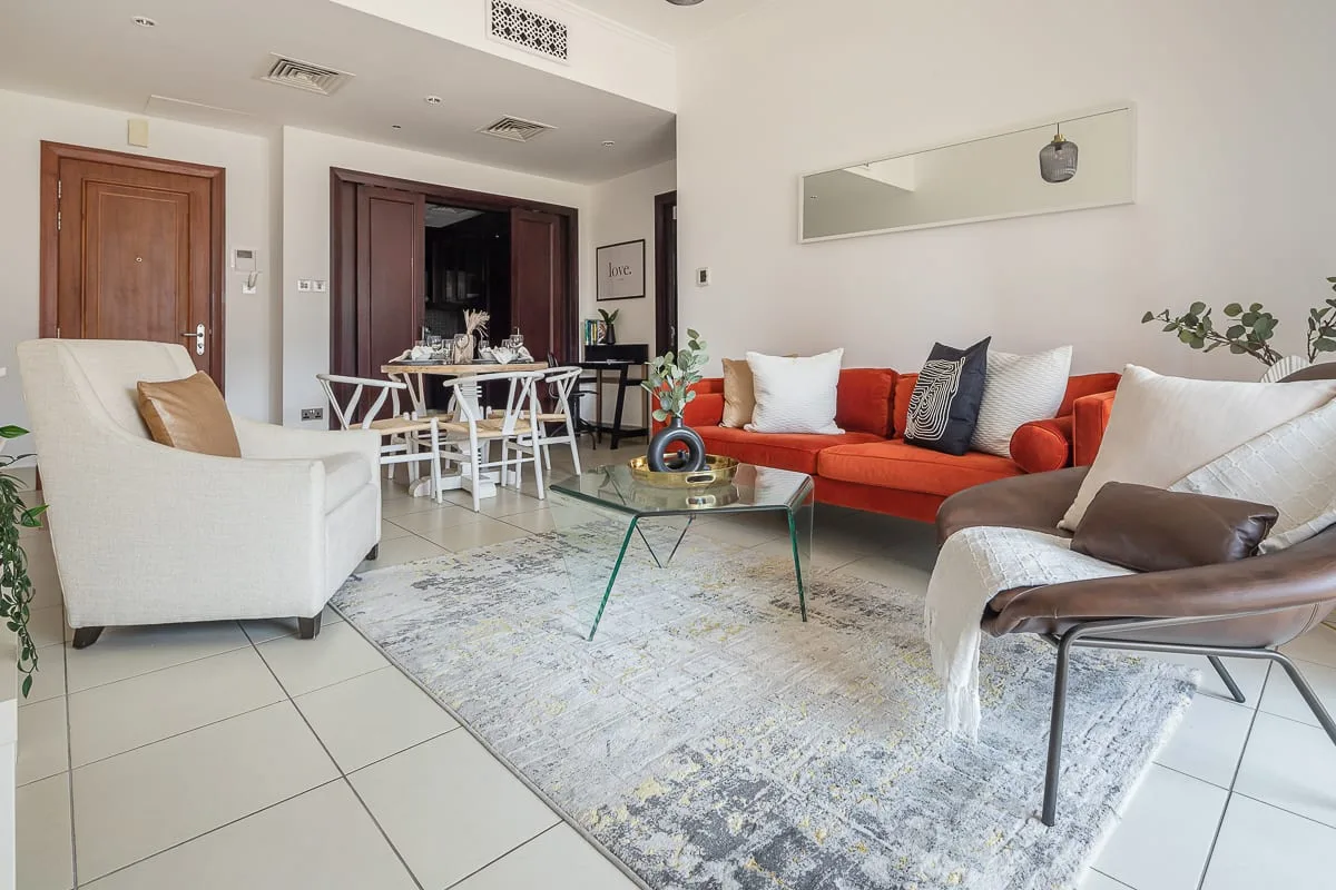 Una sala luminosa con un sofá naranja y una mesa de centro de vidrio.