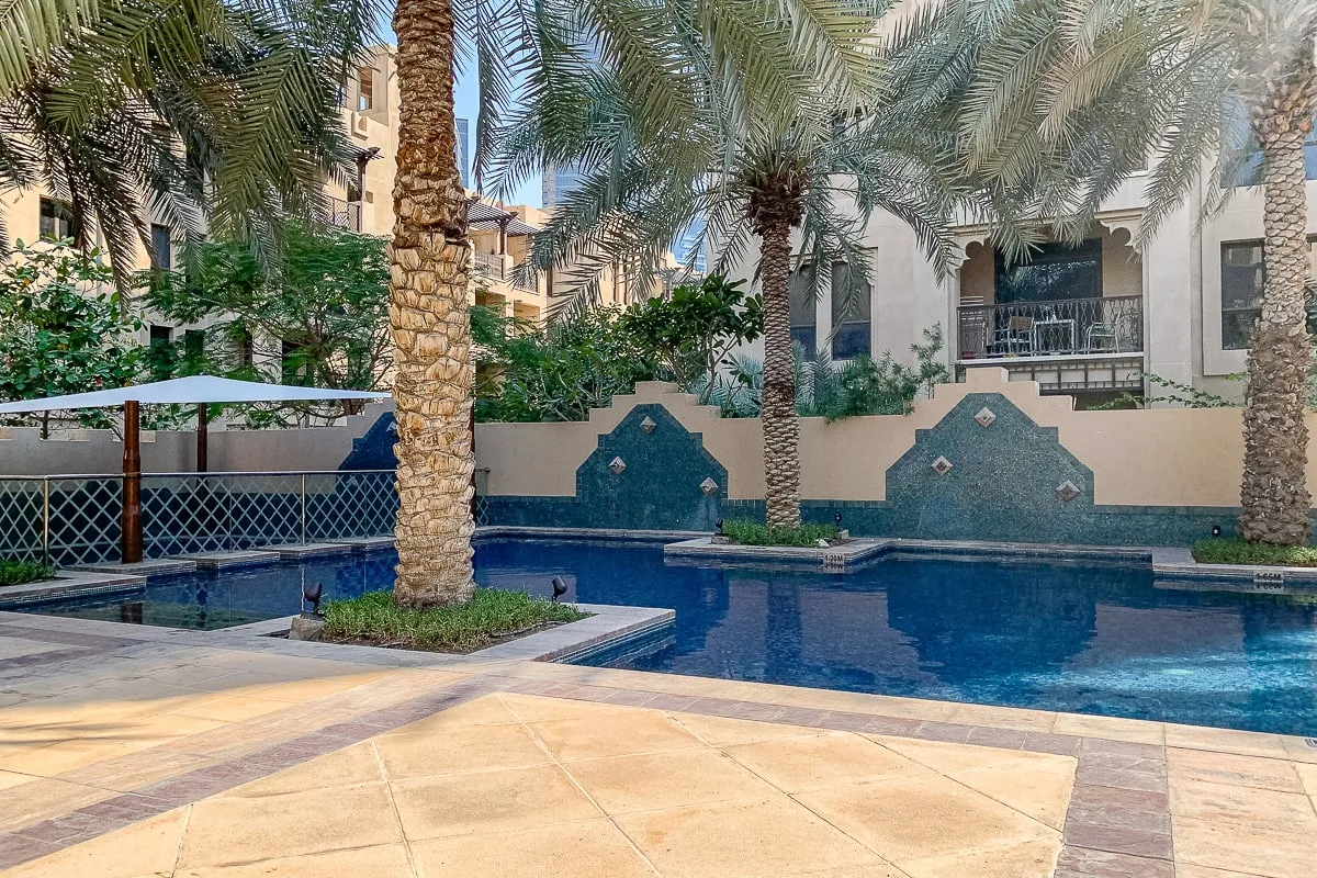 Una piscina en un patio rodeada de palmeras y zonas pavimentadas.