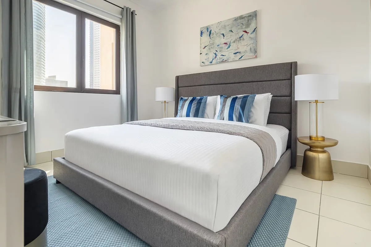 Un dormitorio con una cama bien arreglada, cojines azules y una ventana grande.