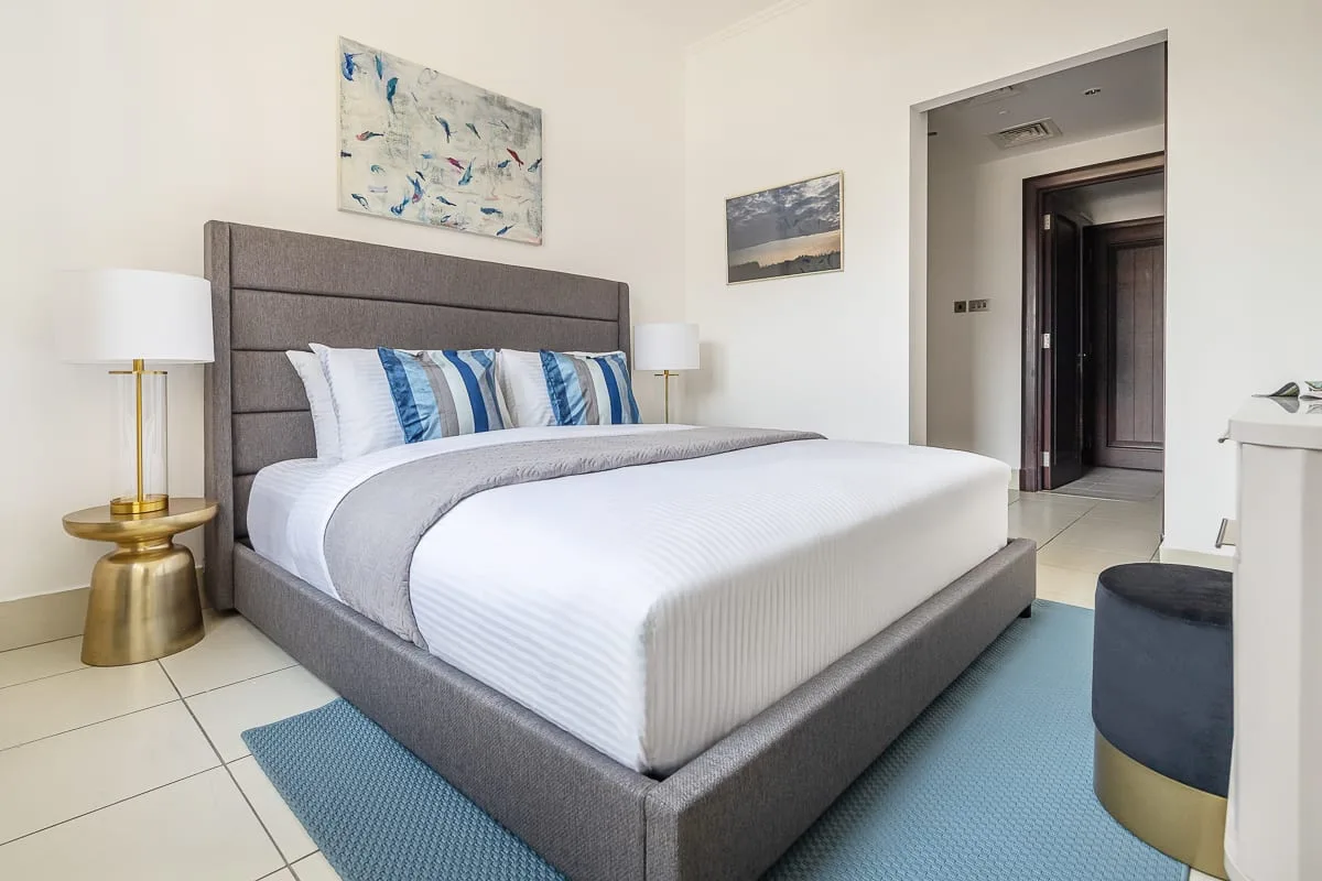 Un dormitorio con una cama grande, una alfombra azul y cuadros en las paredes.