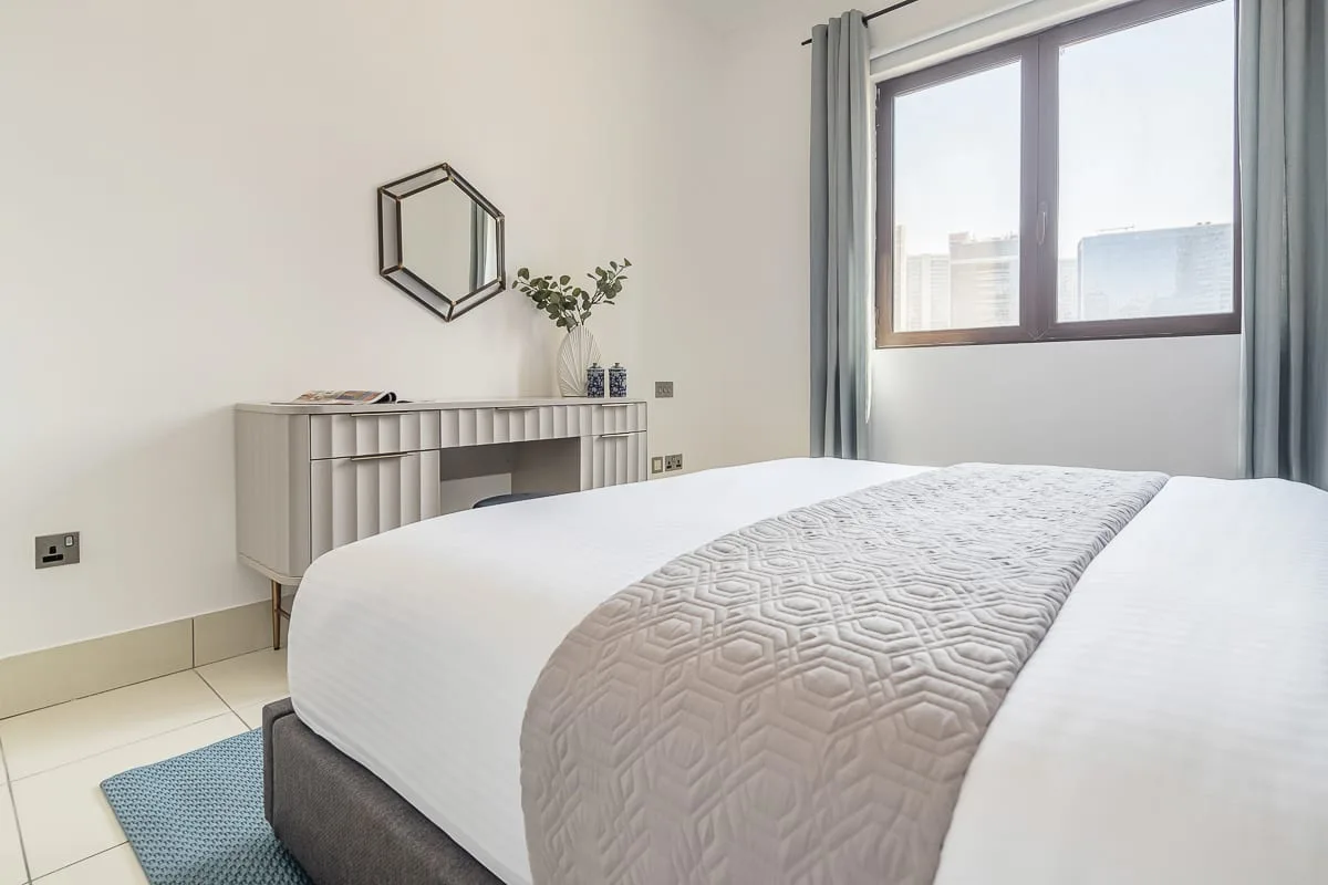 Un dormitorio luminoso con una cama bien tendida y una ventana grande.