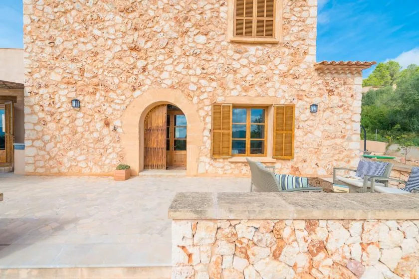 A stone house opens onto a paved patio with outdoor seating.