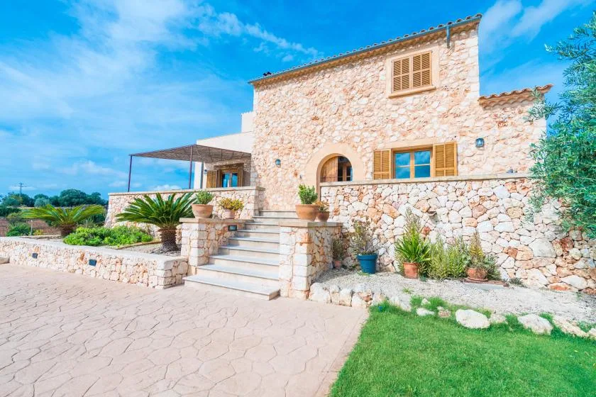 A stone house exterior with a paved walkway, steps, and a small lawn.