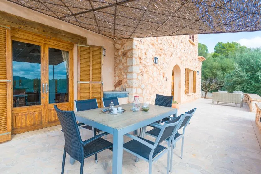 A shaded outdoor dining area with a table and seating beside a stone building.