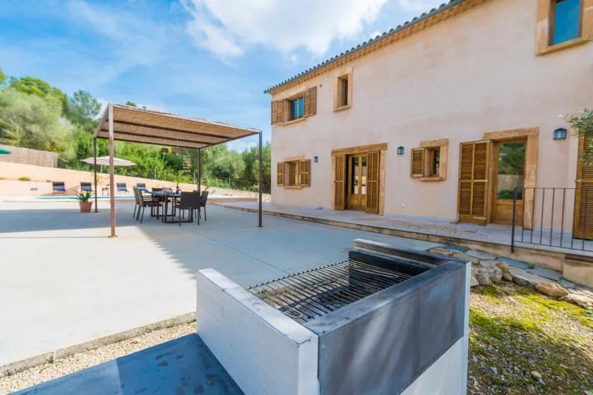 A paved outdoor patio beside a house, with shaded seating and a built-in grill.
