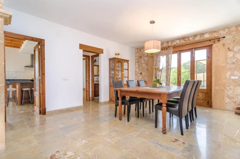 A dining room with a wooden table and chairs beside large windows.