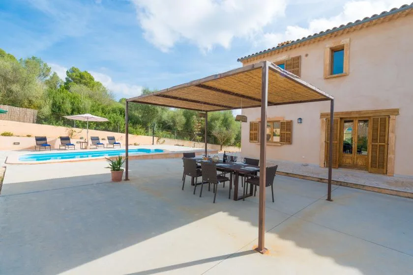 A poolside patio with shaded dining seating and a two-story house.