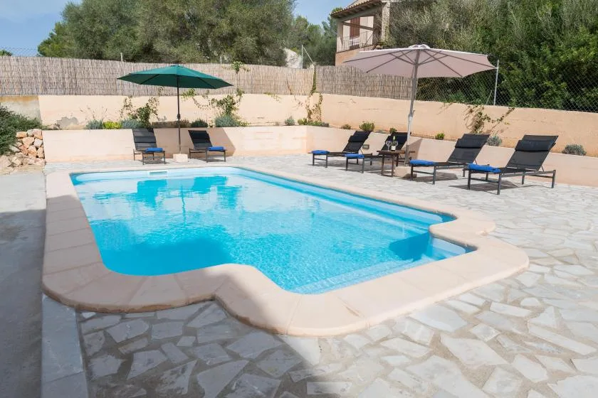 An outdoor swimming pool is surrounded by lounge seating and umbrellas.