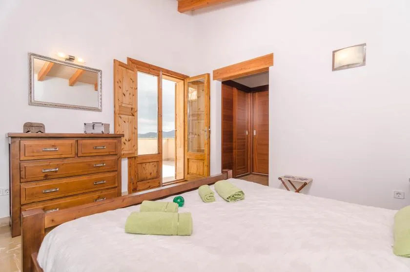A bedroom with a wooden dresser, wardrobes, and folded towels on the bed.