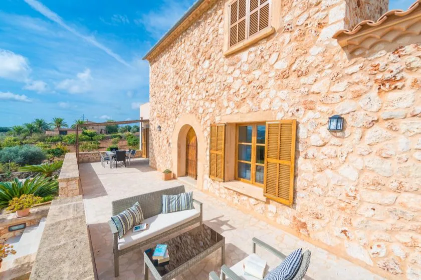 A sunny stone patio with outdoor seating and wooden shutters.