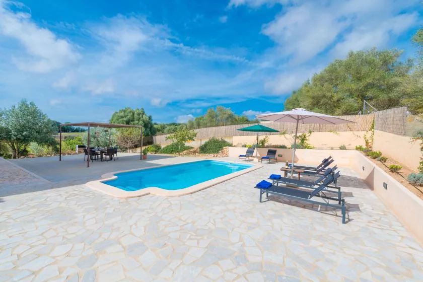 An outdoor pool sits beside a stone-paved patio with loungers and umbrellas.