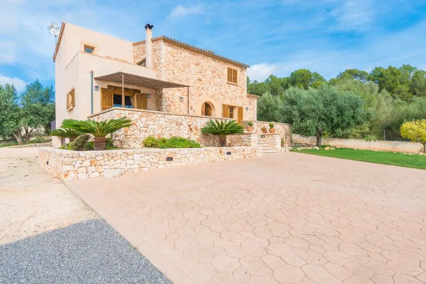A stone-and-stucco house stands beside a broad paved courtyard.