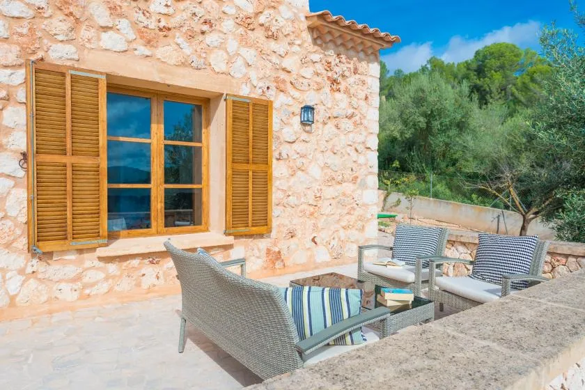 A stone house patio with outdoor seating beside a shuttered window.