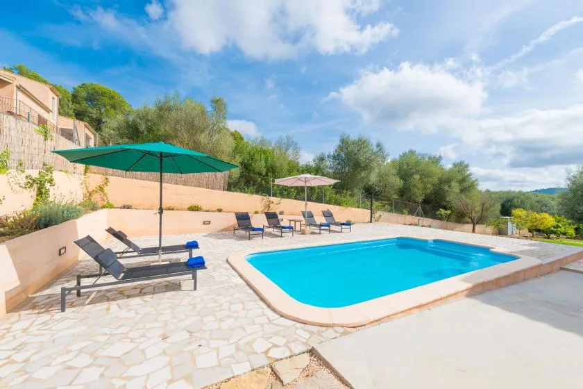 An outdoor swimming pool is surrounded by lounge seating and umbrellas.
