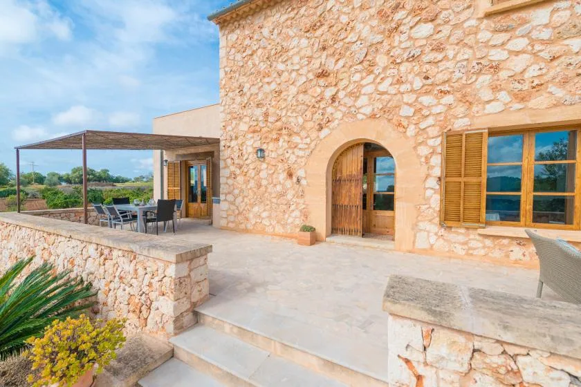 A stone house opens onto a sunny patio with a shaded seating area.