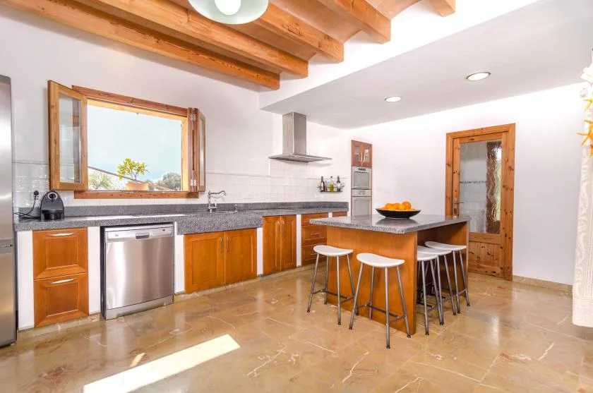 A bright kitchen with wooden cabinetry, a central island, and exposed ceiling beams.
