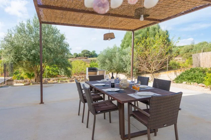 An outdoor dining area with a table and seating beneath a shaded pergola.
